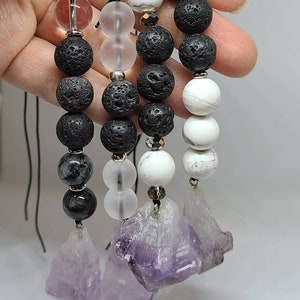 May include: Four beaded necklaces with amethyst crystal pendants. Each necklace features black lava rock beads, clear glass beads, and white and grey beads.