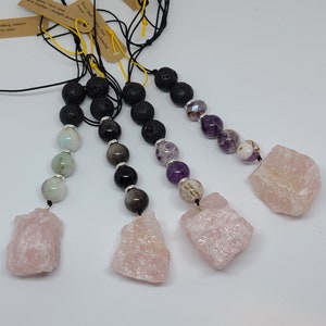 May include: Five crystal necklaces with rose quartz pendants and various gemstone beads. The necklaces are made with black lava beads and have a black cord.