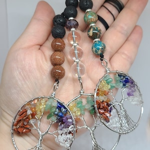 May include: Three silver wire wrapped tree of life charms with different coloured gemstones. The charms are attached to beaded necklaces with lava rock, clear quartz, and brown jasper beads.