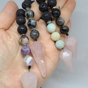 May include: Three pink rose quartz crystal pendulums with black lava rock and other gemstone beads on black cords.