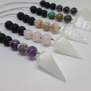 May include: Five white crystal point pendulums with different gemstone beads on a string. The beads include black lava rock, brown and beige agate, turquoise, and pink rose quartz.