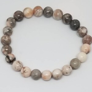May include: A bracelet made of pink, grey, and white stones. The stones are round and have a marbled pattern.