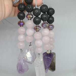 May include: Four crystal necklaces featuring black lava beads, rose quartz beads, and amethyst crystal pendants. The necklaces are strung on grey cords.