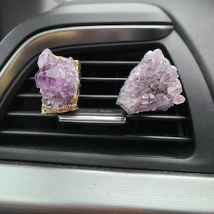 May include: Two amethyst crystal car air fresheners. One is gold-trimmed and the other is plain. Both are purple and have a cluster of crystals.