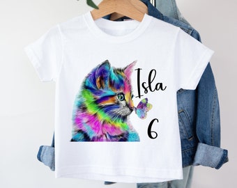 Può includere: Maglietta bianca con un'illustrazione di un gatto colorato e una farfalla. Il testo "Isla 6" è stampato sulla maglietta.