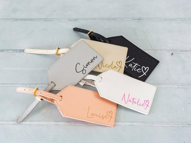 Puede incluir: Cinco etiquetas de equipaje de cuero con herrajes dorados y nombres personalizados: Simon, Nicola, Katie, Natalie y Louise. Cada etiqueta tiene un peque&ntilde;o s&iacute;mbolo de coraz&oacute;n.
