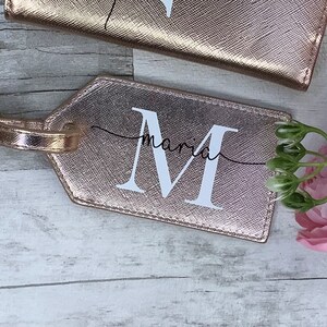 Pu&ograve; includere: Etichetta per bagagli in oro rosa con una M bianca e il nome Maria scritto in corsivo.