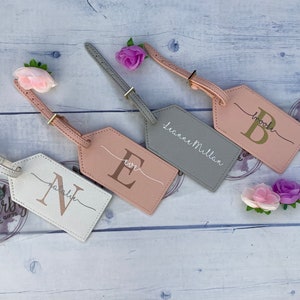 4 pu luggage tags. One white with rose gold initial and silver name, pink with rose gold initial and white name, grey tag with white name, pink tag with gold initial and grey name. All with gold buckle.