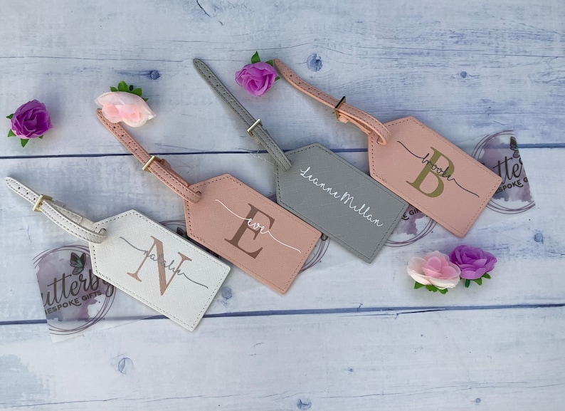 4 pu luggage tags. One white with rose gold initial and silver name, pink with rose gold initial and white name, grey tag with white name, pink tag with gold initial and grey name. All with gold buckle.