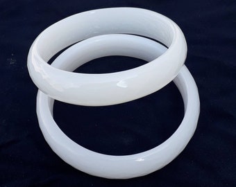 May include: Two white bangle bracelets made of smooth, glossy ceramic. The bracelets are stacked on top of each other.