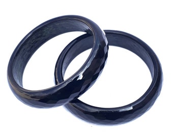 May include: Two black bangle bracelets with a faceted design. The bracelets are made of a smooth, polished material.