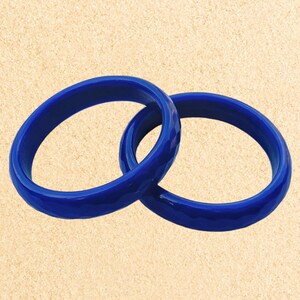 May include: Two blue bangle bracelets made of smooth, glossy plastic. The bracelets are stacked on top of each other.