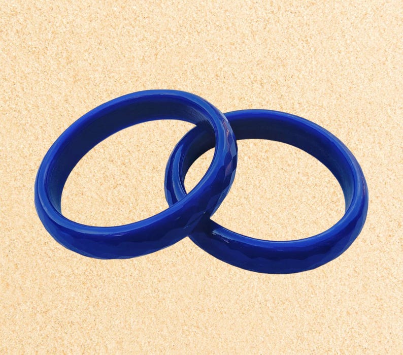 May include: Two blue bangle bracelets made of smooth, glossy plastic. The bracelets are stacked on top of each other.