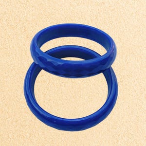 May include: Two blue bangle bracelets, one with a smooth finish and the other with a textured finish. The bracelets are stacked on top of each other.
