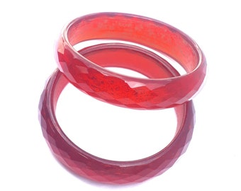 May include: Two red plastic bangles with a faceted design. The bangles are stacked on top of each other.