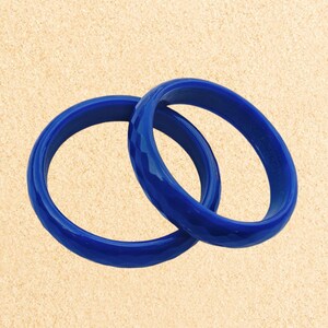 May include: Two blue bangle bracelets made of plastic. The bracelets are stacked on top of each other.