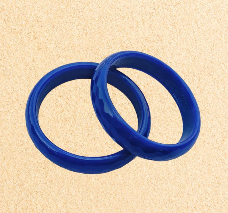 May include: Two blue bangle bracelets made of plastic. The bracelets are stacked on top of each other.