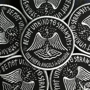 May include: A close-up of several black and white embroidered patches with the text "Be not unkind to strangers, lest they be angels in disguise".