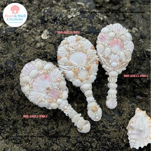 Könnte beinhalten: Drei handgefertigte Dekorationsspiegel für den Strand. Jeder Spiegel ist mit einer Vielzahl von Muscheln, Perlen und kleinen Schalen verziert. Die Spiegel haben ein weißes und rosa Farbschema. Die Griffe sind ebenfalls mit Muscheln und Perlen verziert.
