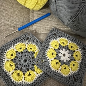 Peut inclure: Deux carrés au crochet avec un motif de fleur gris, blanc et jaune. Les carrés sont faits de fil et d'un crochet.