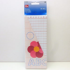 May include: A pack of squared paper, 87 by 62 centimetres, with a blue and white grid pattern. The pack has a pink flower design with a yellow centre and the letters ABC in blue.