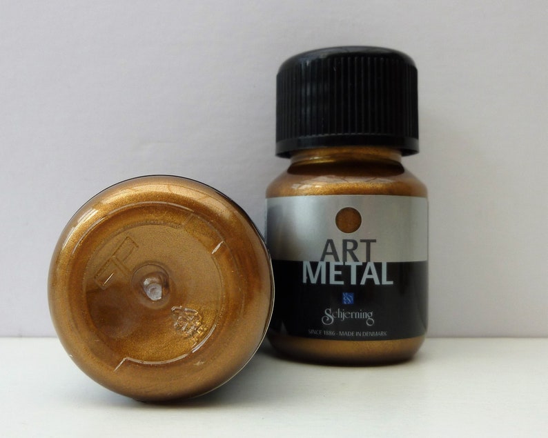 K&ouml;nnte beinhalten: Eine kleine Flasche goldfarbener Metallic-Farbe mit der Aufschrift "Art Metal" von Schjerning. Die Flasche wurde in D&auml;nemark hergestellt.