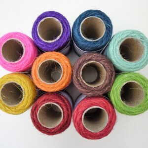 May include: Ten spools of colorful twine, each wound around a cardboard tube. The twine is a natural fiber, and the colors are bright and vibrant. The spools are arranged in a circle, with the ends of the twine extending out from the center.