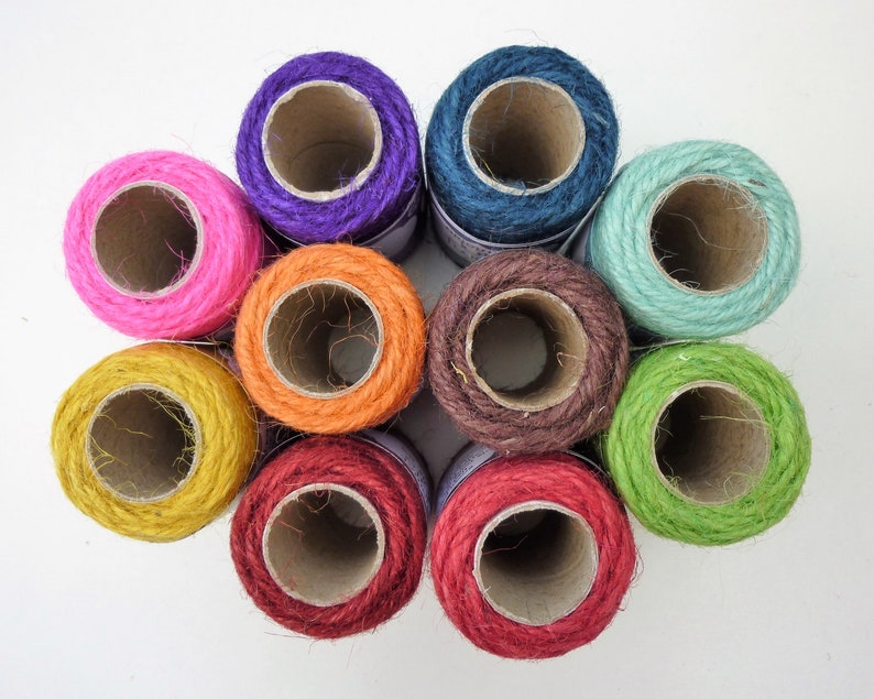 May include: Ten spools of colorful twine, each wound around a cardboard tube. The twine is a natural fiber, and the colors are bright and vibrant. The spools are arranged in a circle, with the ends of the twine extending out from the center.