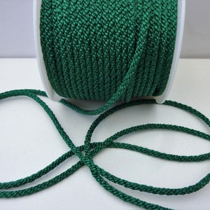 May include: A spool of dark green braided cord. The cord is wound around a white spool and there is a length of cord lying on a white surface.