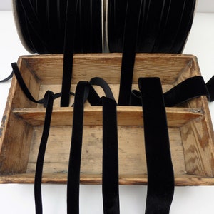 May include: A wooden box filled with black velvet ribbon. The ribbon is arranged in a criss-cross pattern.
