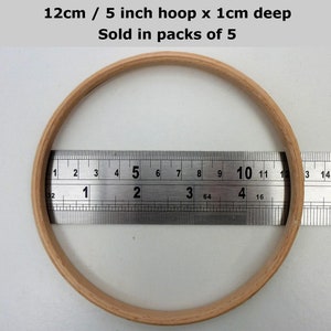 May include: A wooden embroidery hoop with a diameter of 5 inches and a depth of 1 cm. The hoop is being measured with a ruler. The text "12cm / 5 inch hoop x 1cm deep Sold in packs of 5" is visible in the image.