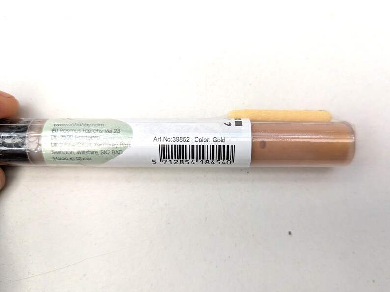 May include: A close-up of a gold cosmetic tube with the text "Art No. 39852 Color: Gold" and a barcode. The tube is made in China.