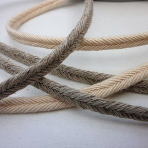 May include: Two spools of braided cord, one in a natural beige colour and the other in a dark brown colour. The cords are woven in a herringbone pattern.