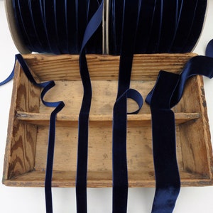 Puede incluir: Cuatro carretes de cinta de terciopelo azul oscuro en una caja de madera. La cinta está dispuesta en forma de cruz.