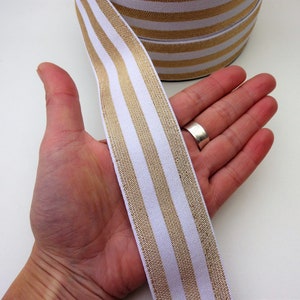 May include: White elastic ribbon with gold stripes. The ribbon is approximately 2.5 cm wide.