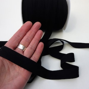 Puede incluir: Cinta el&aacute;stica negra, de aproximadamente 2,5 cm de ancho, mostrada en una mano. La cinta es suave y flexible, y es ideal para proyectos de costura.