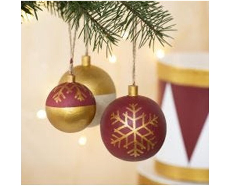 May include: Three Christmas ornaments with a gold and burgundy color scheme. The ornaments are decorated with a snowflake design in gold paint.