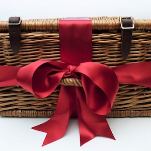 Puede incluir: Cesta de picnic de mimbre con tapa con bisagras, asegurada con correas y hebillas de cuero marr&oacute;n. Una gran cinta de raso rojo vibrante est&aacute; atada alrededor de la cesta, formando un lazo decorativo. La cesta est&aacute; vac&iacute;a.
