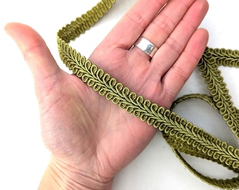 May include: Olive green decorative trim with a looped design. The trim is made of a woven material and is shown in a close-up view. The trim is flexible and appears to be new. The trim is shown in a person's hand.