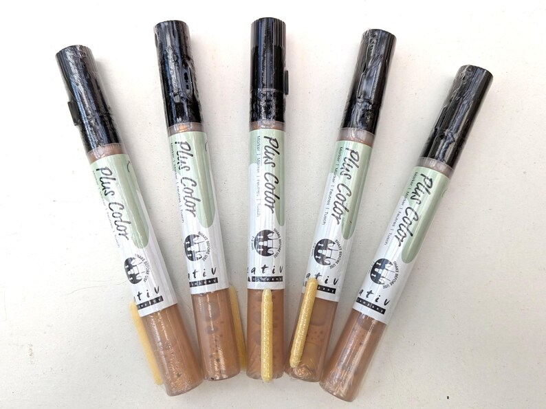 May include: Five gold metallic markers with black caps and the words "Plus Color" printed on the side. The markers are arranged in a fan shape.