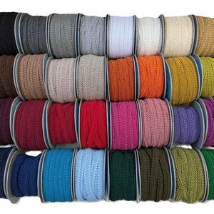 May include: A collection of spools of decorative trim in a variety of colors, including black, gray, white, beige, brown, orange, pink, purple, blue, green, and red. The trim is tightly wound on spools, ready for use in crafting or sewing projects.