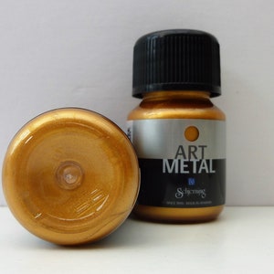 K&ouml;nnte beinhalten: Zwei kleine Flaschen goldener Metallic-Farbe. Die Flaschen sind mit "Art Metal" und dem Schjerning-Logo beschriftet.