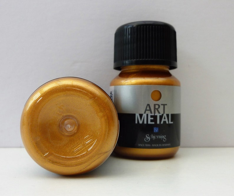 K&ouml;nnte beinhalten: Zwei kleine Flaschen goldener Metallic-Farbe. Die Flaschen sind mit "Art Metal" und dem Schjerning-Logo beschriftet.