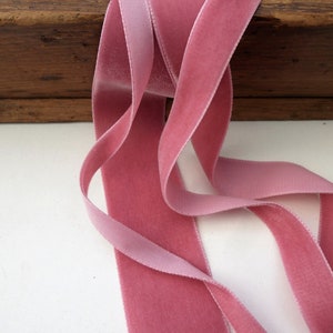 Puede incluir: Primer plano de una cinta de terciopelo rosa. La cinta est&aacute; doblada y drapeada sobre una superficie de madera.