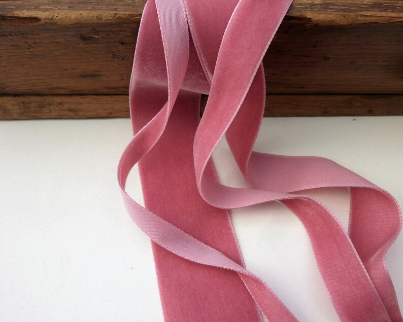 Puede incluir: Primer plano de una cinta de terciopelo rosa. La cinta est&aacute; doblada y drapeada sobre una superficie de madera.