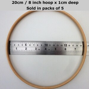 May include: A wooden embroidery hoop with a diameter of 8 inches or 20 centimeters. The hoop is 1 centimeter deep. The hoop is being measured with a ruler. The text on the image reads "20cm / 8 inch hoop x 1cm deep Sold in packs of 5".
