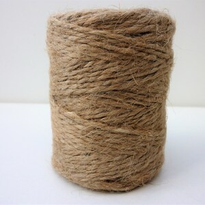 May include: A roll of natural brown twine, made from jute fiber, is wound tightly on a spool.