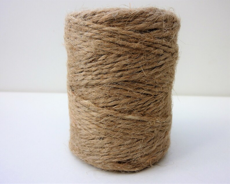 May include: A roll of natural brown twine, made from jute fiber, is wound tightly on a spool.