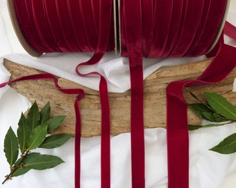 May include: Four spools of deep red velvet ribbon, each about 1/4 inch wide, are displayed on a white surface. The ribbon is arranged in a way that shows its texture and color.