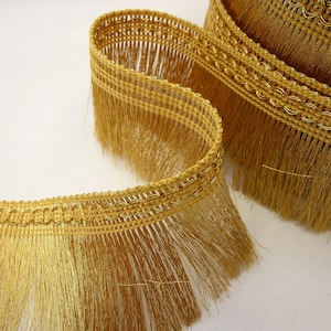 May include: Gold fringe trim with a woven chain design. The fringe is approximately 2.5 cm long.
